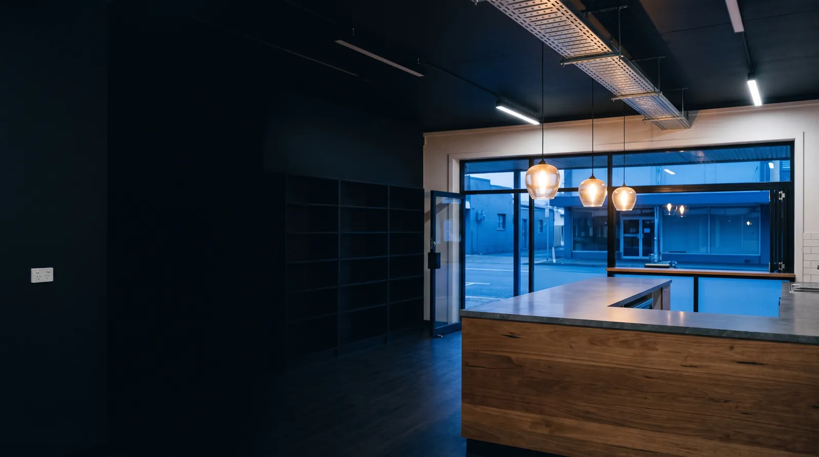 A shop interior at dusk with pendant lights over a timber counter