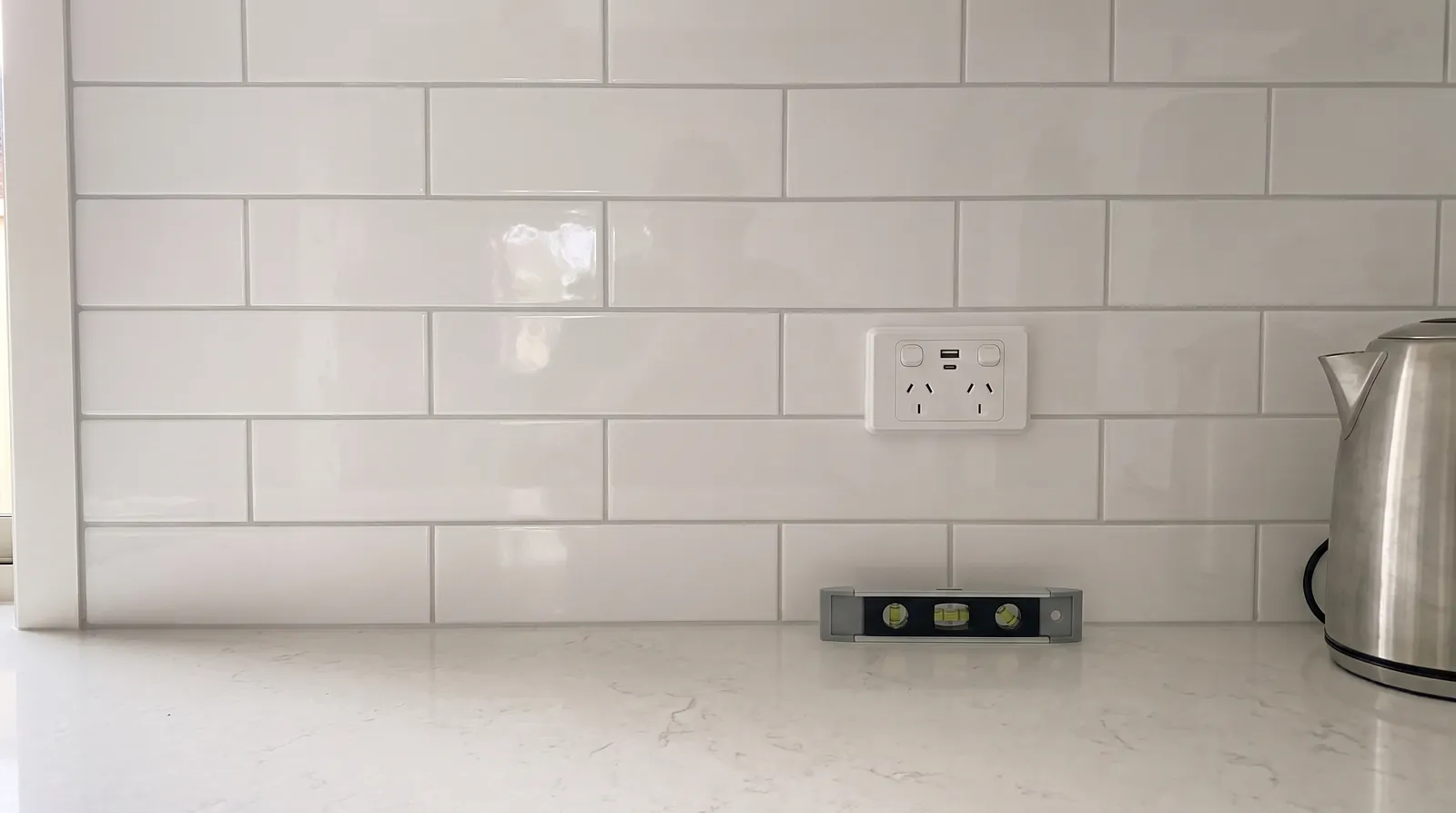 A double power point with USB ports on a white tiled kitchen splashback